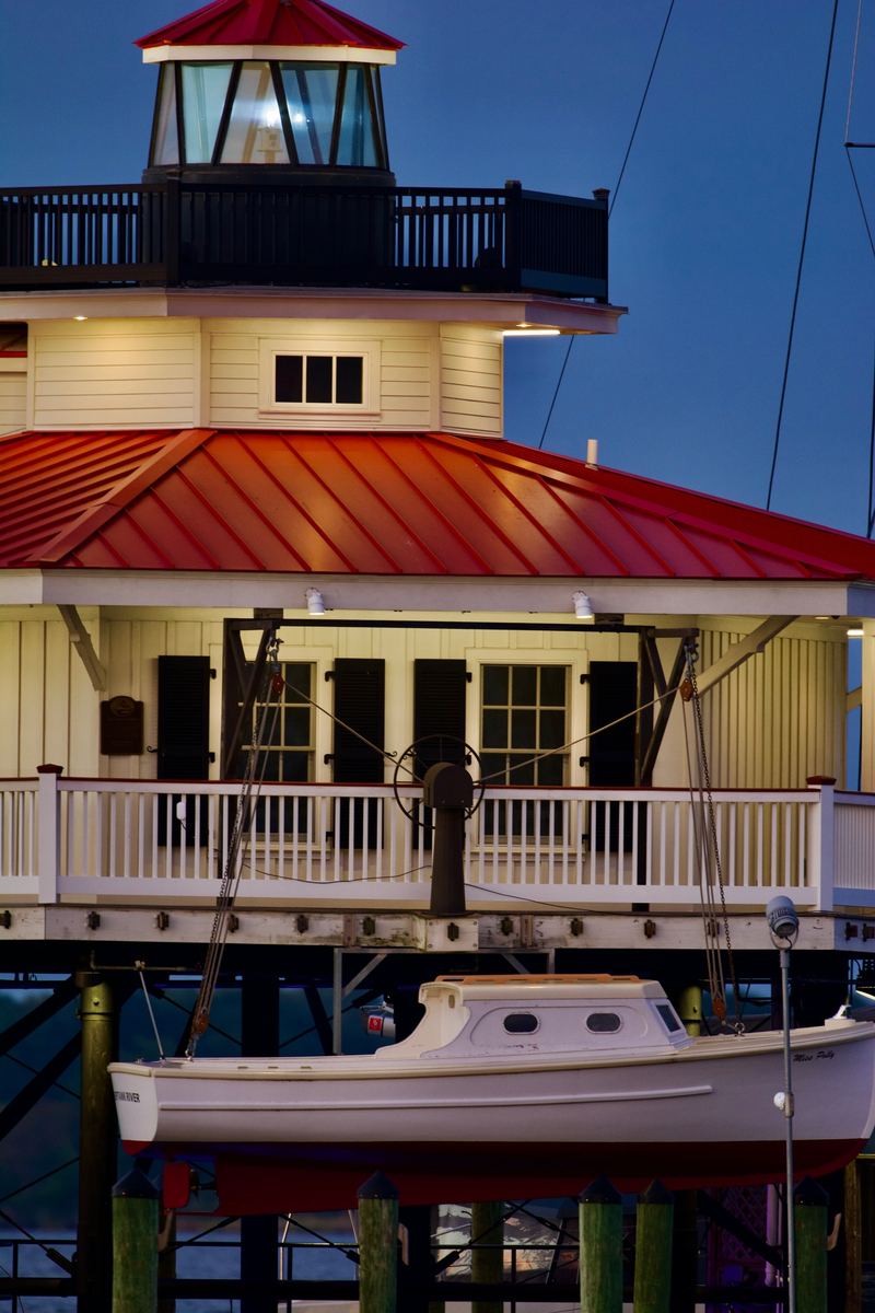 The screw-pile lighthouse on the Cambridge waterfront at dusk, lit windows above a moored workboat.